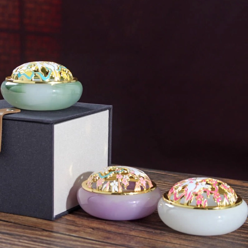 Collection of three handcrafted nine-tailed fox incense burners in jade green, lavender purple, and white jade-style crystal glass with decorative cloisonne lids, side view on wooden display