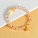 Nine-tailed fox lotus charm bracelet with incense ash liuli glass beads in pale pink, featuring gold fox charm and lotus pendant on white desk