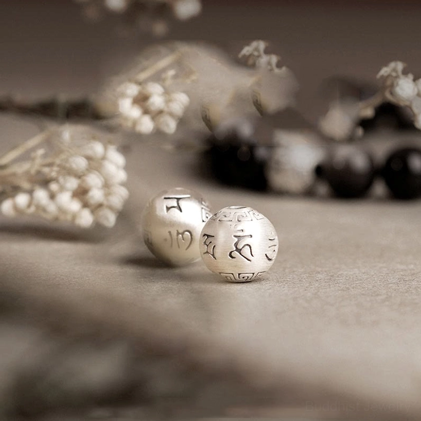 Loose Silver Sheen Obsidian beads and engraved sterling silver mantra charm beads displayed on neutral background with dried florals