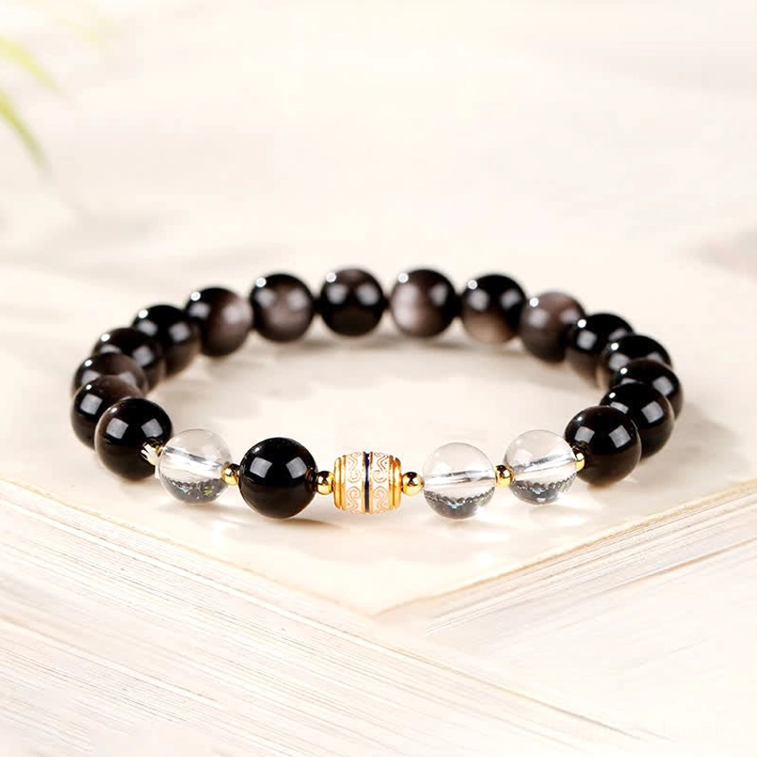 Black obsidian Buddhist bracelet resting on stacked books, showcasing mixed bead sizes, clear spacers and protective stone qualities