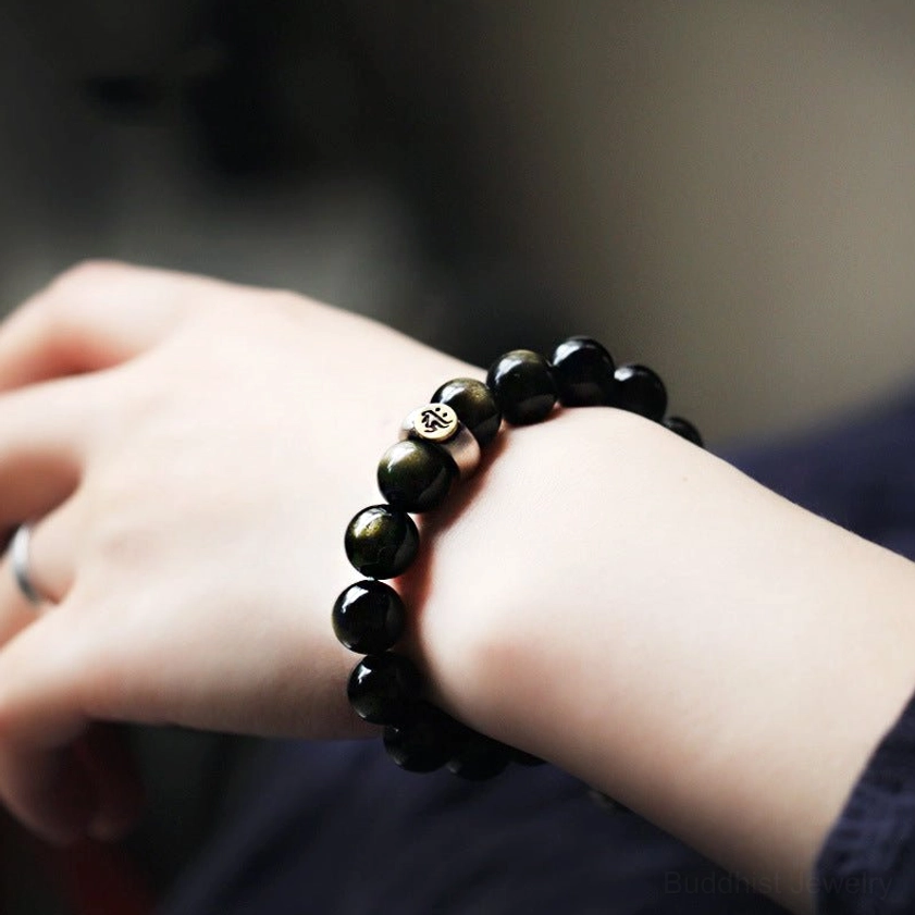 Obsidian natal Buddha bracelet on wrist with embossed metal prayer bead accents