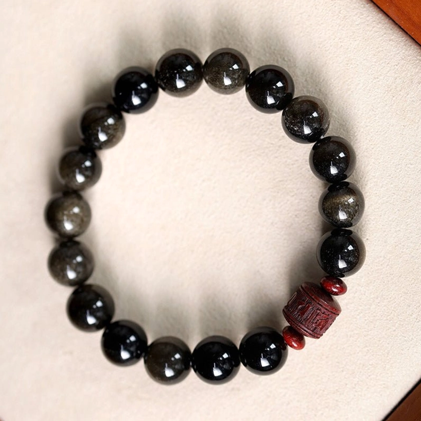 Black obsidian with golden shimmer bracelet with carved focal bead resting on luxury gift box jewelry lining