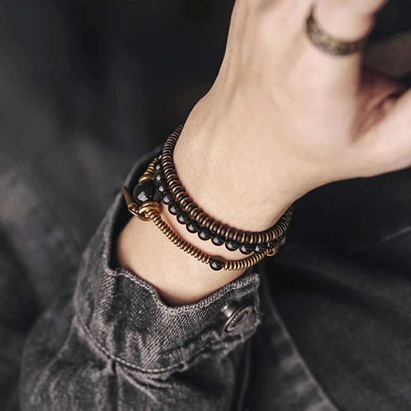 Close-up wearing shot of triple wrap obsidian bracelet on wrist with hand details, showing fitted multi-layer beaded design with bronze accents