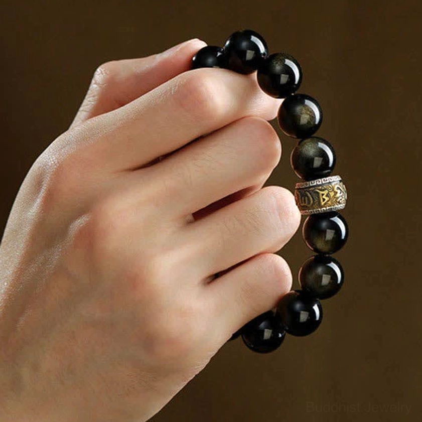 Hand-held gold sheen obsidian bracelet with engraved metal spacer and red pixiu charm detail