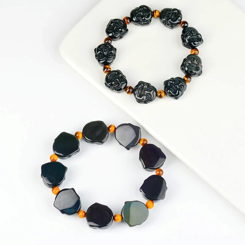 Two Buddhist bracelets comparison on white tray, showing carved laughing Buddha style and smooth obsidian bead variations