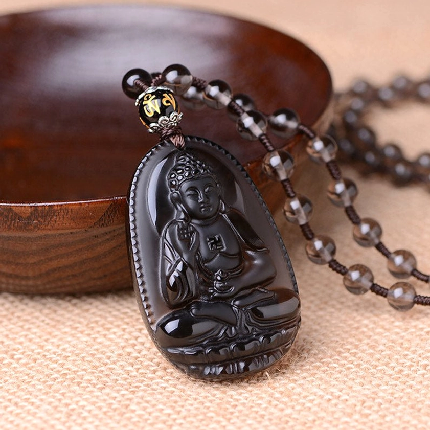 Dark brown obsidian Buddha pendant carved with dharma hand gesture, front-bottom angle on natural fabric