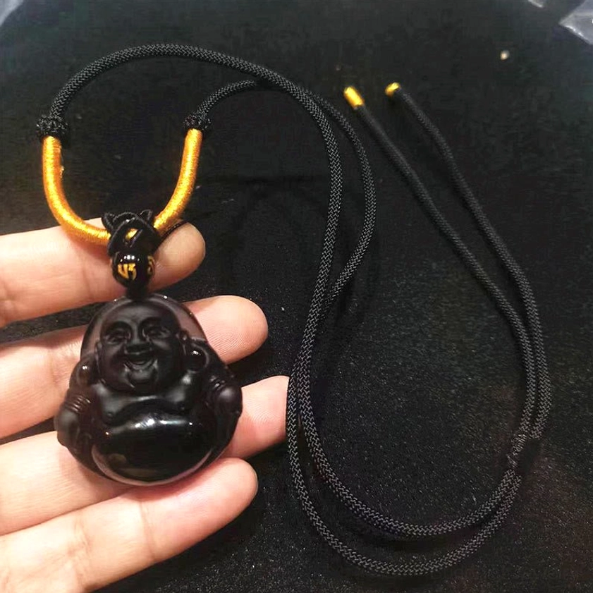 Buddha pendant necklace held in hand side view on black fabric with gold-accented woven rope