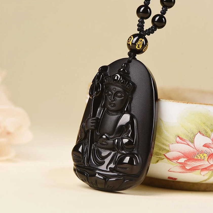 Black obsidian Buddha pendant displayed next to lotus ceramic container showing artistic craftsmanship