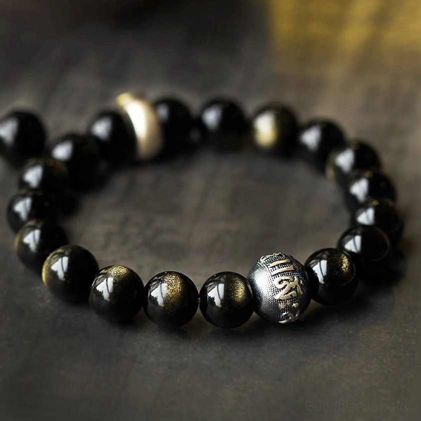 Close-up of obsidian natal Buddha bracelet showing carved metal prayer beads and gemstone detail