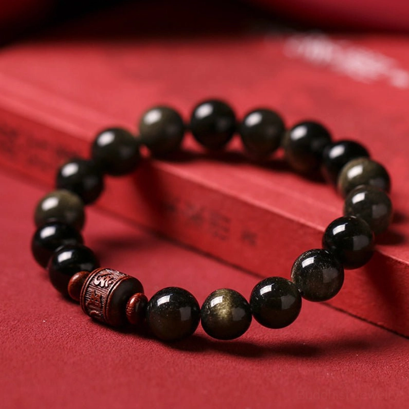 Rainbow and Gold Sheen Obsidian Buddhist bracelet on red background with book prop, displaying black beads with golden and iridescent sheen