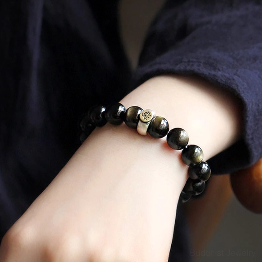 Side view of gold obsidian Buddhist bracelet worn on wrist with dark fabric background