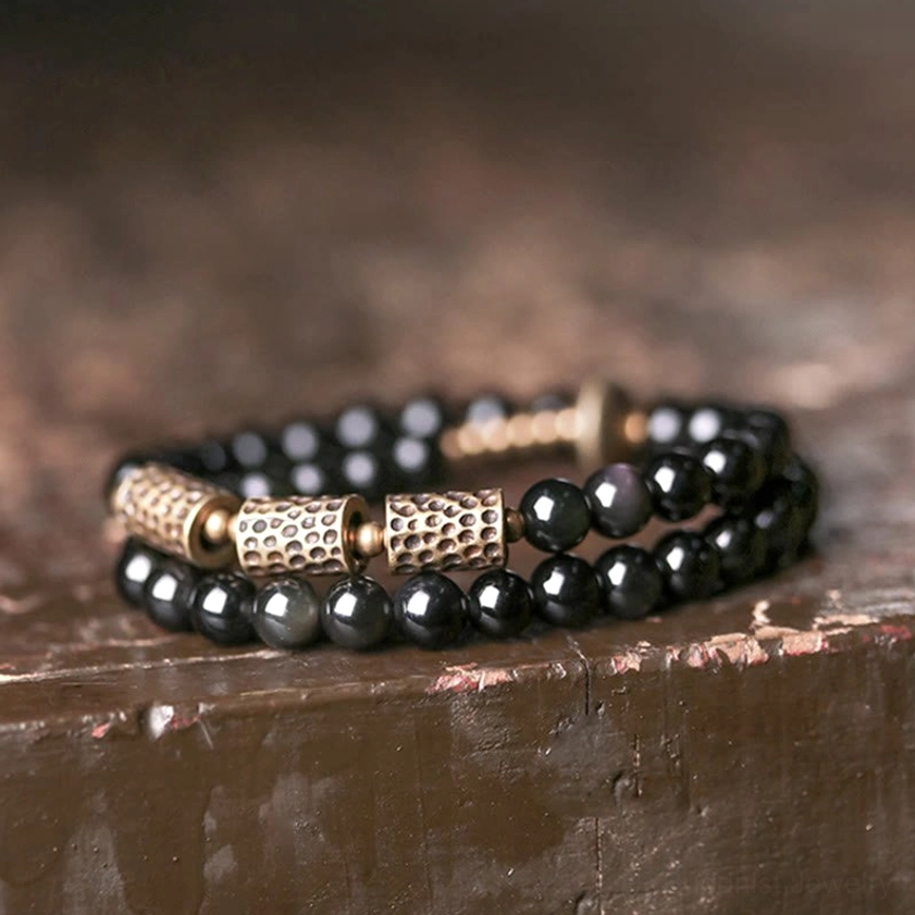 Side close-up of double wrap beaded bracelet with fine black obsidian beads and hammered bronze metal spacers on rustic wooden surface