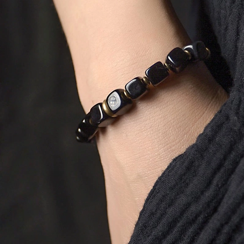 Worn black obsidian copper bracelet on wrist showing branded accent bead and brass hardware close-up
