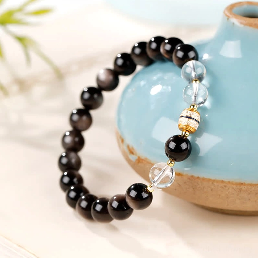 Black silver sheen obsidian Buddhist bracelet with hand-painted Dzi bead, clear glass spacers and gold accents, close-up side angle