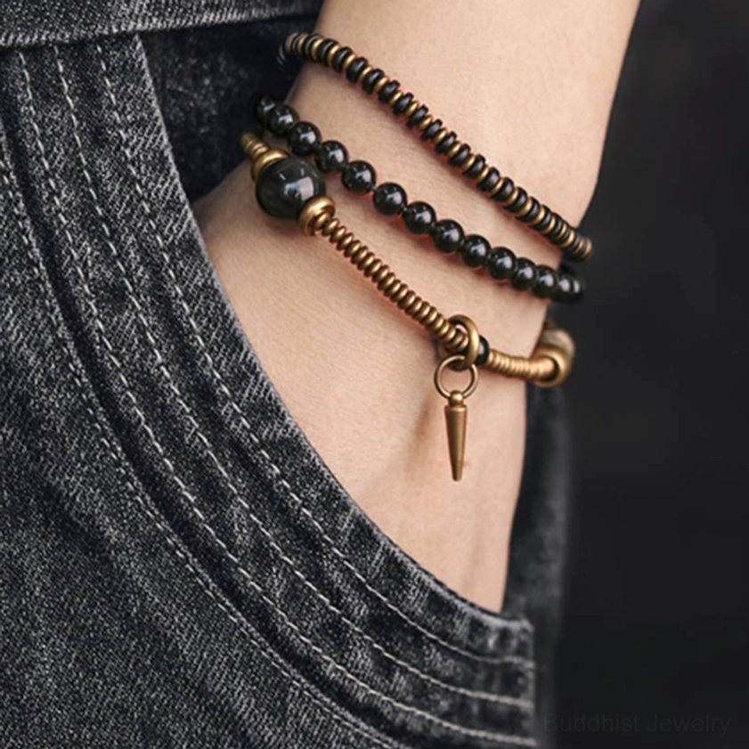Multi-layer beaded healing bracelet on wrist near denim pocket, featuring slim three-layer stacked design with bronze hardware