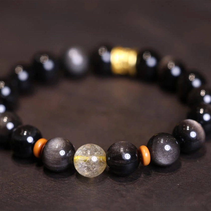 Silver Sheen Obsidian Om Mani Padme Hum bracelet with golden rutilated quartz center bead and crystal accents on dark background