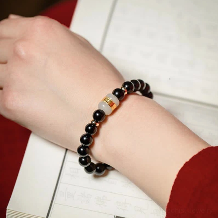 Black obsidian and jade om mani padme hum bracelet worn on left wrist next to vintage Chinese calligraphy books, demonstrating spiritual significance