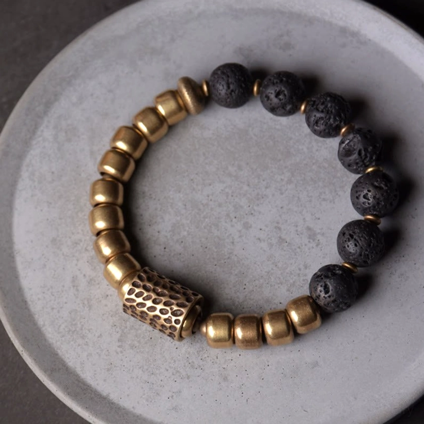 Handmade healing bracelet featuring lava rock and brass beads on ceramic plate, showing brushed brass spacers and porous black lava stone texture