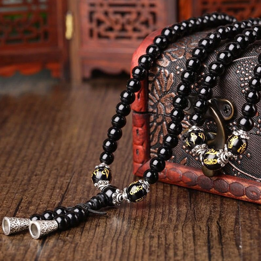 Full-length Black Obsidian Buddhist mala bracelet with extended tassel and carved metal ornaments displayed on wooden table