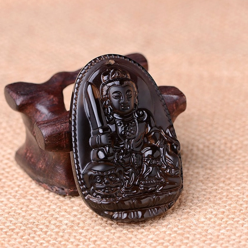 Polished black obsidian Manjushri Bodhisattva pendant necklace displayed on wooden stand with linen cloth