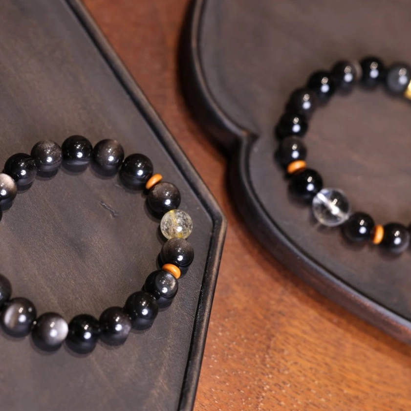 Silver Sheen Obsidian Buddhist bracelet with golden rutilated quartz bead on wooden surface showing bead details