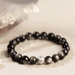 Silver Sheen Obsidian Om Mani Padme Hum Buddhist bracelet with engraved sterling silver mantra beads, flat lay top view on neutral background