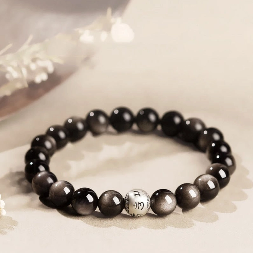 Silver Sheen Obsidian Om Mani Padme Hum Buddhist bracelet with engraved sterling silver mantra beads, flat lay top view on neutral background