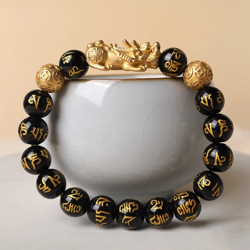 12mm black obsidian Pixiu wealth bracelet resting on white ceramic cup showing full beaded design with gold accents
