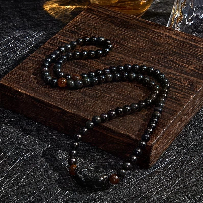 Long obsidian beaded strand with carved Pixiu charm and tiger eye stone accents, side view on wooden background