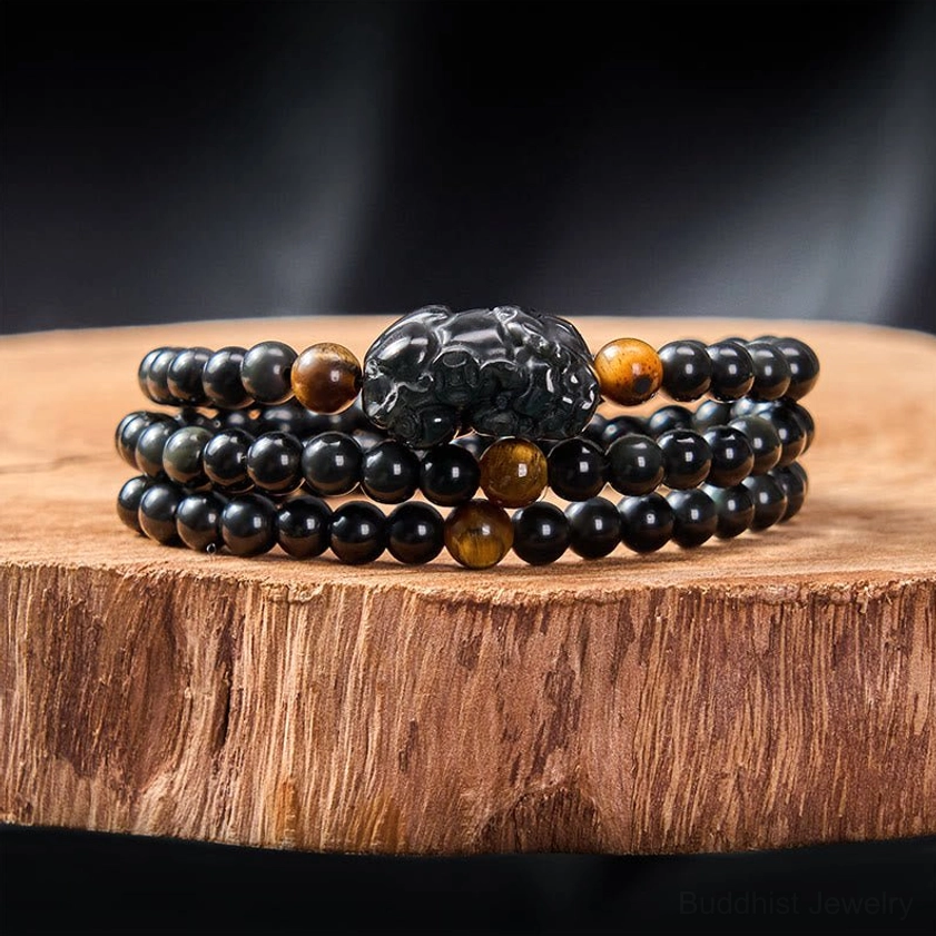 Multi-layer black obsidian Pixiu bracelet triple-wrap design on wooden slab showing hand-carved prosperity charm