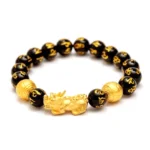 Black obsidian Pixiu wealth bracelet flat lay overhead view with gold Pixiu charm and engraved mantra beads on white background