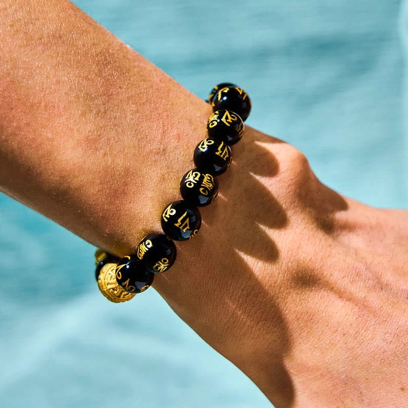 Partial view of black obsidian Pixiu bracelet on human wrist showing engraved mantra beads and gold spacers
