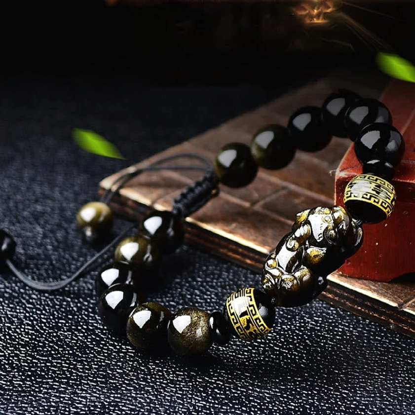 3/4 side angle of gold sheen obsidian Pixiu bracelet with full beaded design and protective charm on wooden coaster