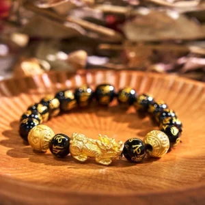 Black obsidian PiXiu wealth bracelet with gold Sanskrit mantra beads and charm, flat lay on wooden tray