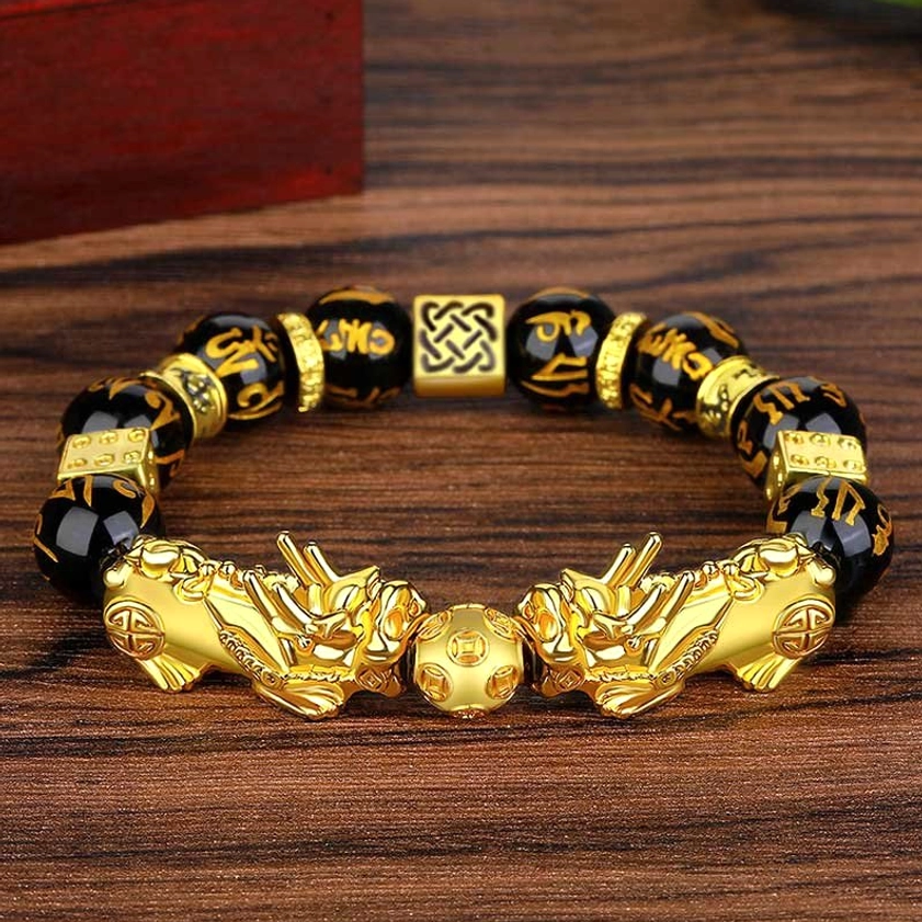 Black obsidian Pixiu Buddhist bracelet on wooden surface displaying paired golden Pixiu charms and Sanskrit engraved beads - side angle view