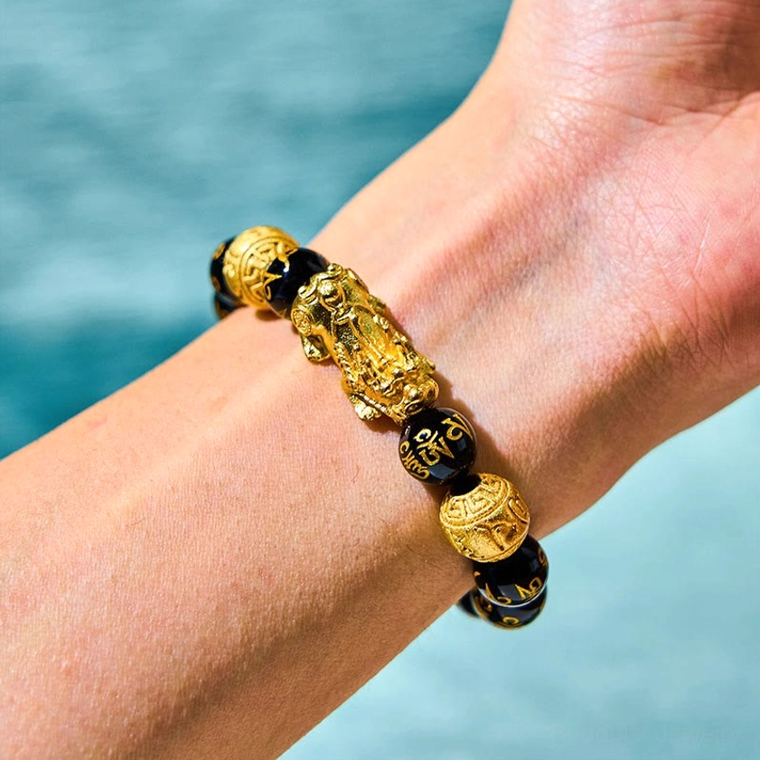 Pixiu obsidian bracelet worn on wrist with gold Sanskrit engraved beads and golden Pixiu charm, close-up side view