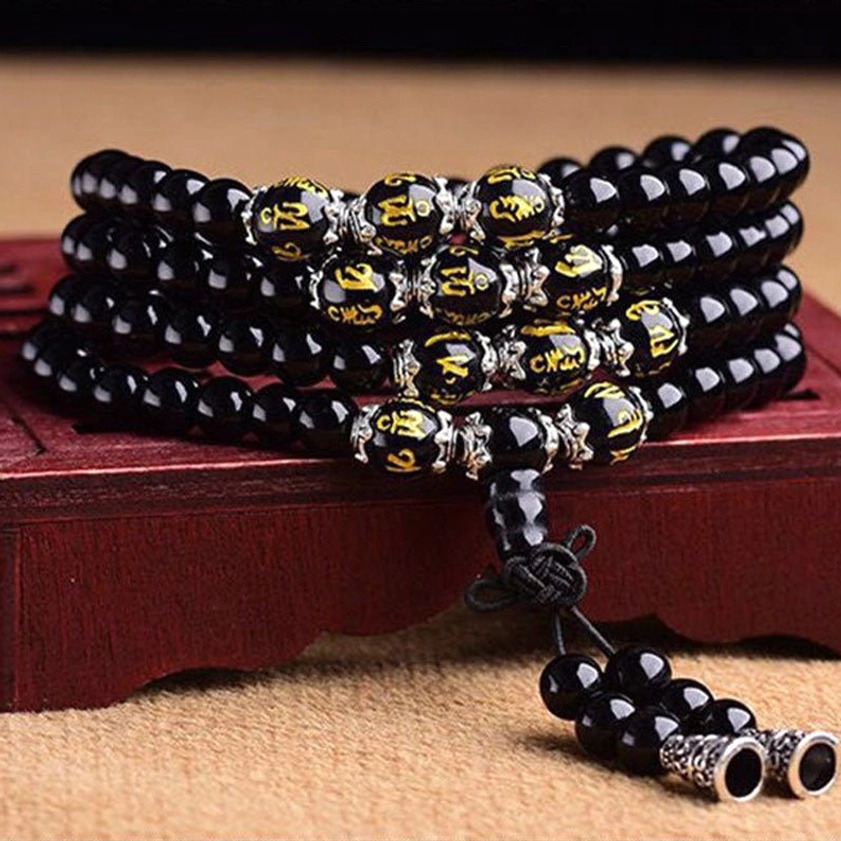 Close-up of 108-bead Black Obsidian Buddhist prayer mala with golden Om Mani Padme Hum inscribed beads and knotted tassel with metal charms