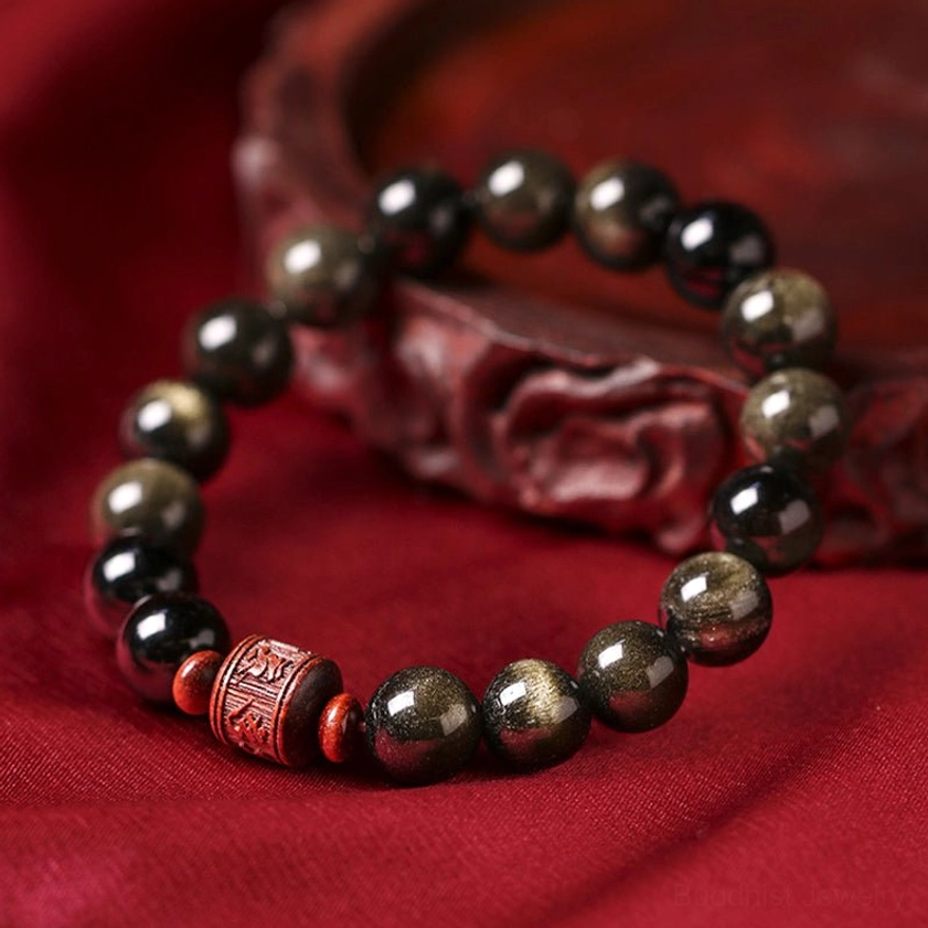 Gold Sheen Obsidian beads with carved wooden ornament prop on red satin, side angle view showing bead surface detail