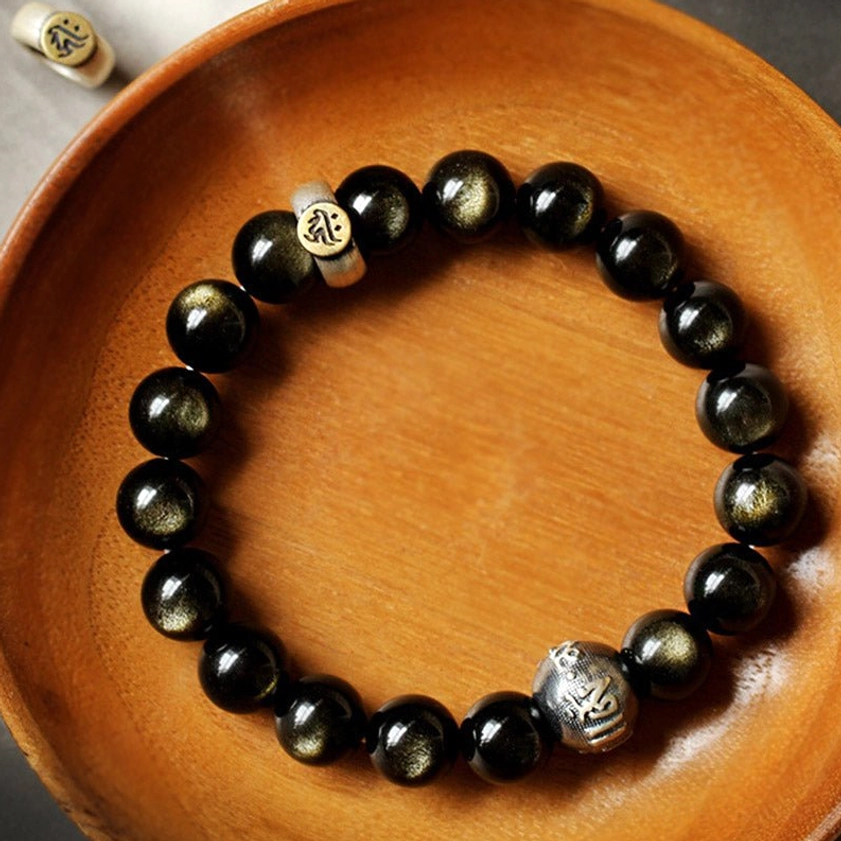 Gold obsidian protection bracelet displayed on wooden surface with sterling silver accents