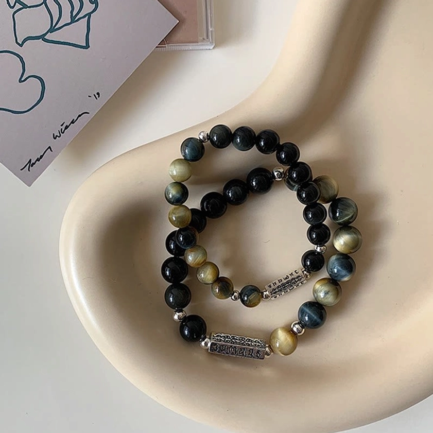Double layer black obsidian and tiger eye protective stone bracelets stacked on cream ceramic tray, matching set with metal spacer details