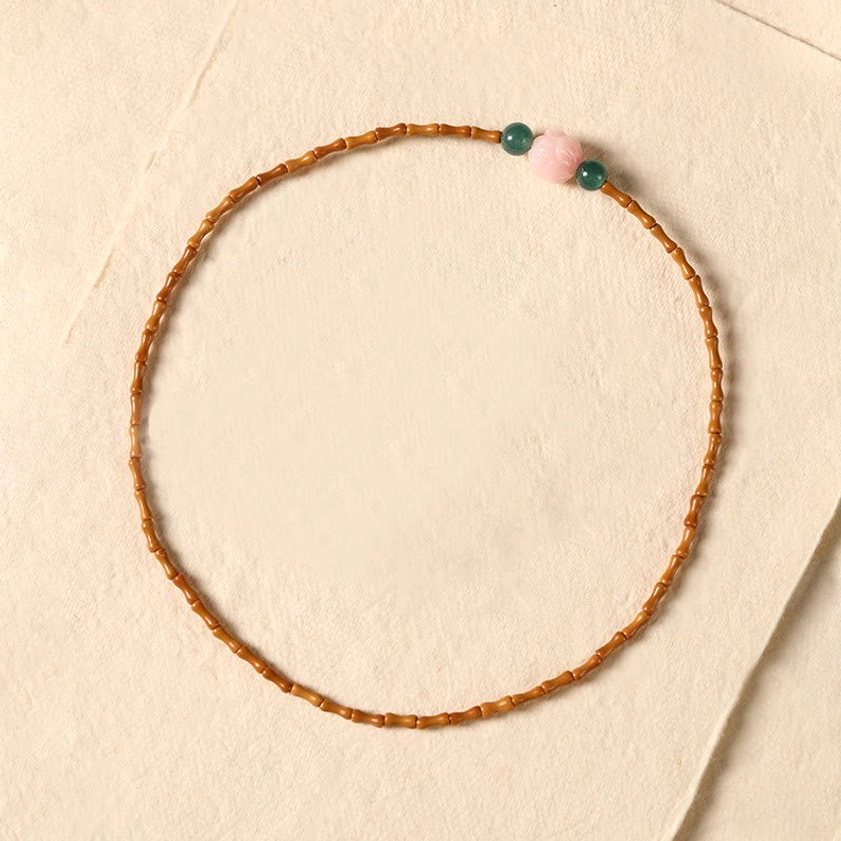 Bamboo olive pit beads with pink lotus and green accent beads displayed on light neutral fabric background