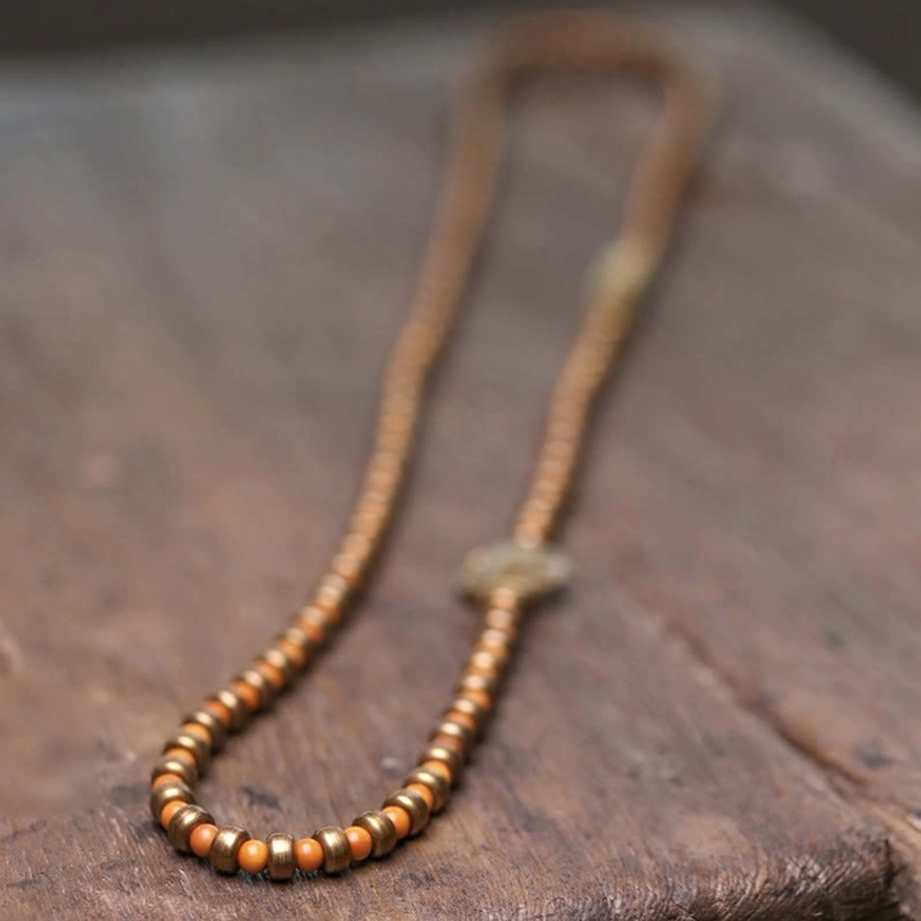 Long strand of natural olive pit beads with central bronze decorative knot - unstrung presentation