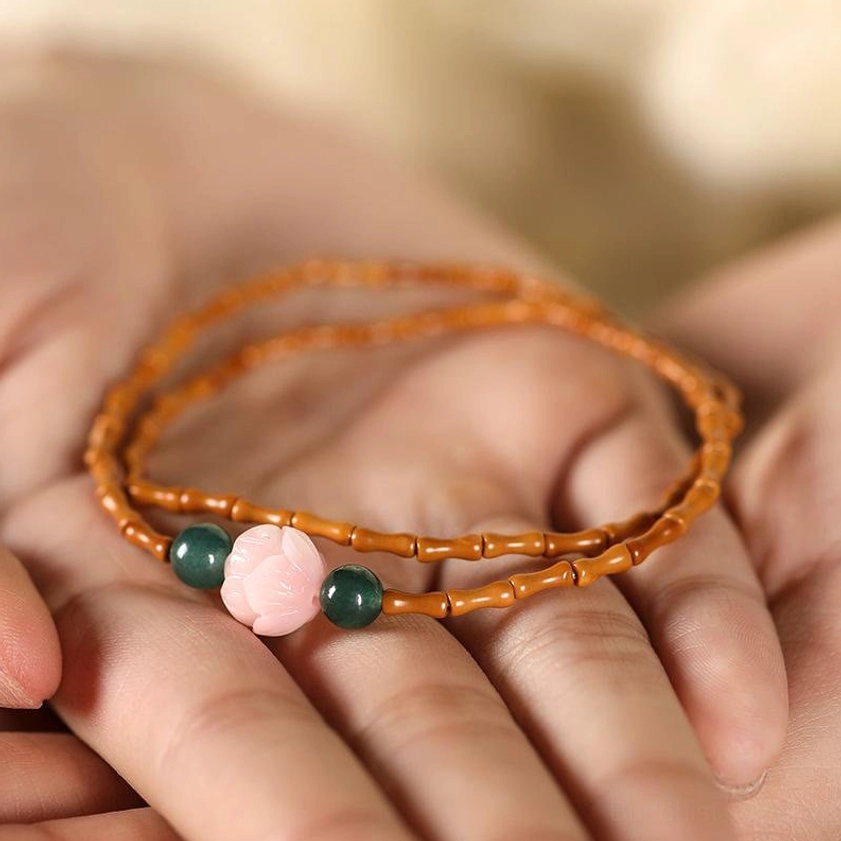 Close-up hand-held view of double strand olive pit lotus beaded bracelet with brown beads and green stone accents