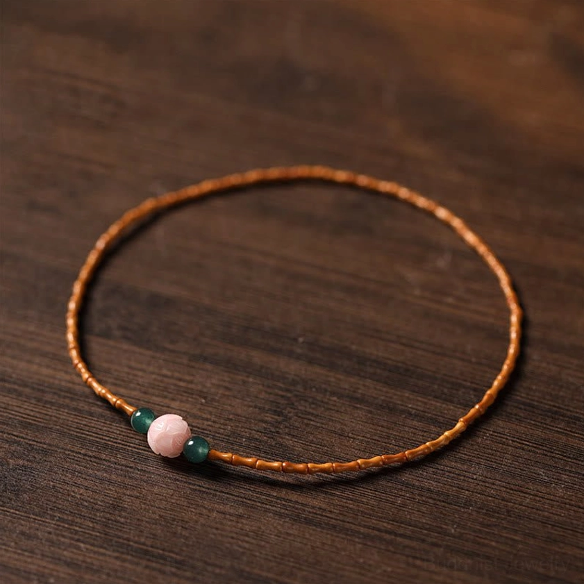 Single strand olive pit lotus bracelet flat lay on dark wooden surface showing bamboo beads and lotus accent