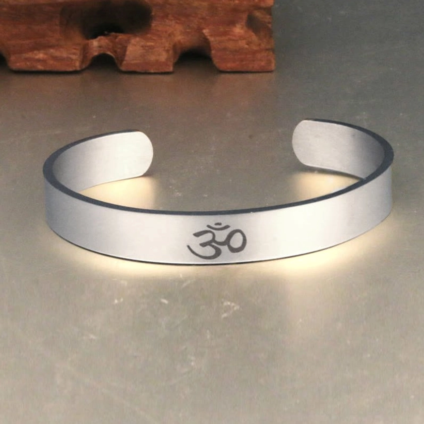 OM symbol open cuff bangle overhead front view, matte silver finish with clear engraving detail