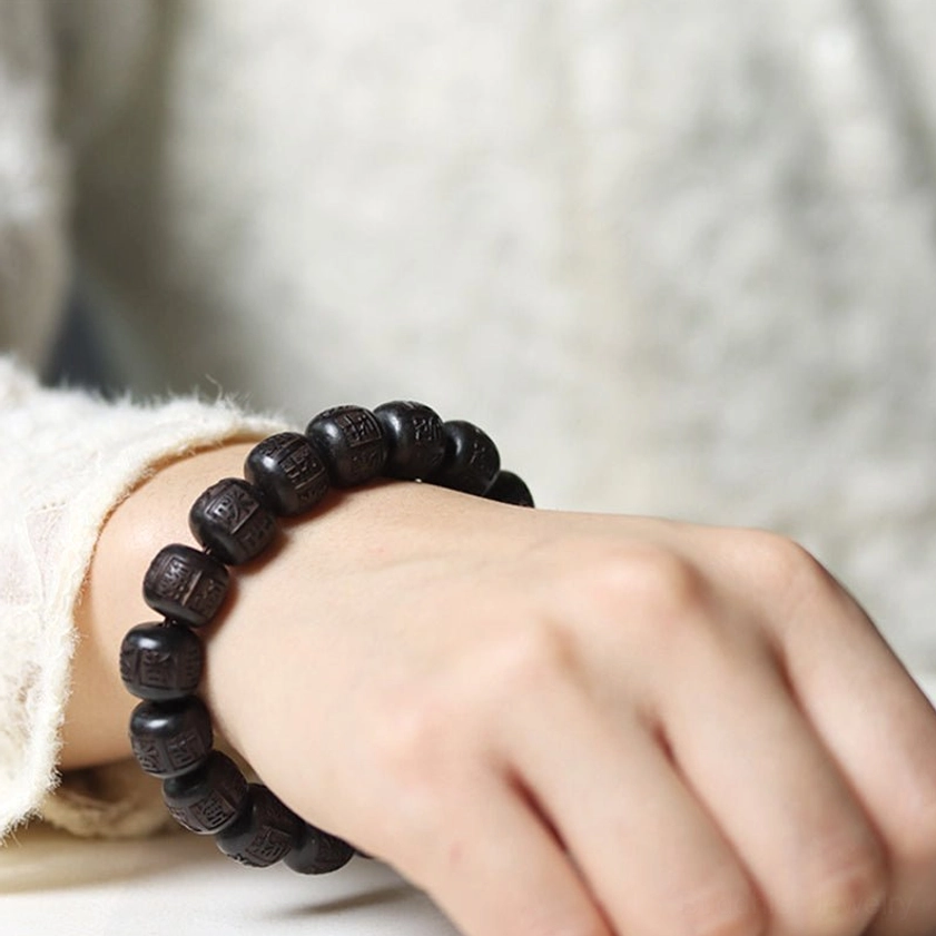 Close-up of ebony wood mantra bracelet on wrist with white sleeve showing crisp engraved text details