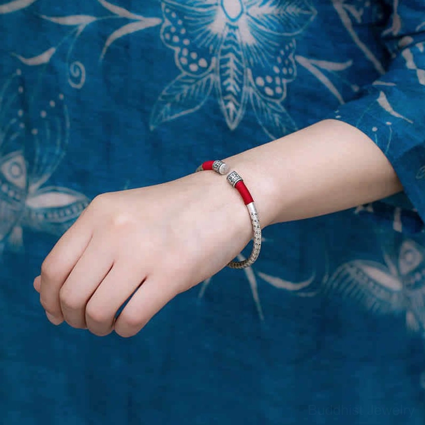 Stacked Om Mani Padme Hum bracelets on wrist, multiple silver and red bangles layered together