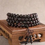 108-bead red sandalwood Om Mani Padme Hum prayer bracelet with sterling silver cloud inlays displayed on carved wooden stand