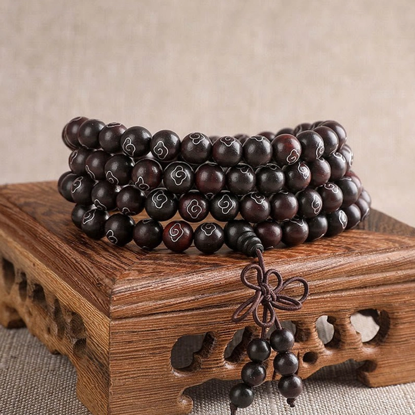 108-bead red sandalwood Om Mani Padme Hum prayer bracelet with sterling silver cloud inlays displayed on carved wooden stand