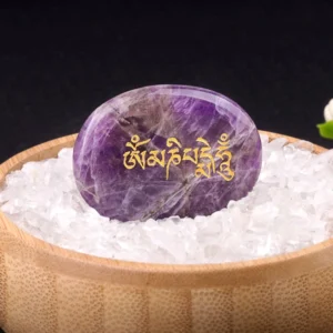 Om Mani Padme Hum amethyst palm stone with golden Sanskrit engraving displayed in wooden bowl with crystal gravel
